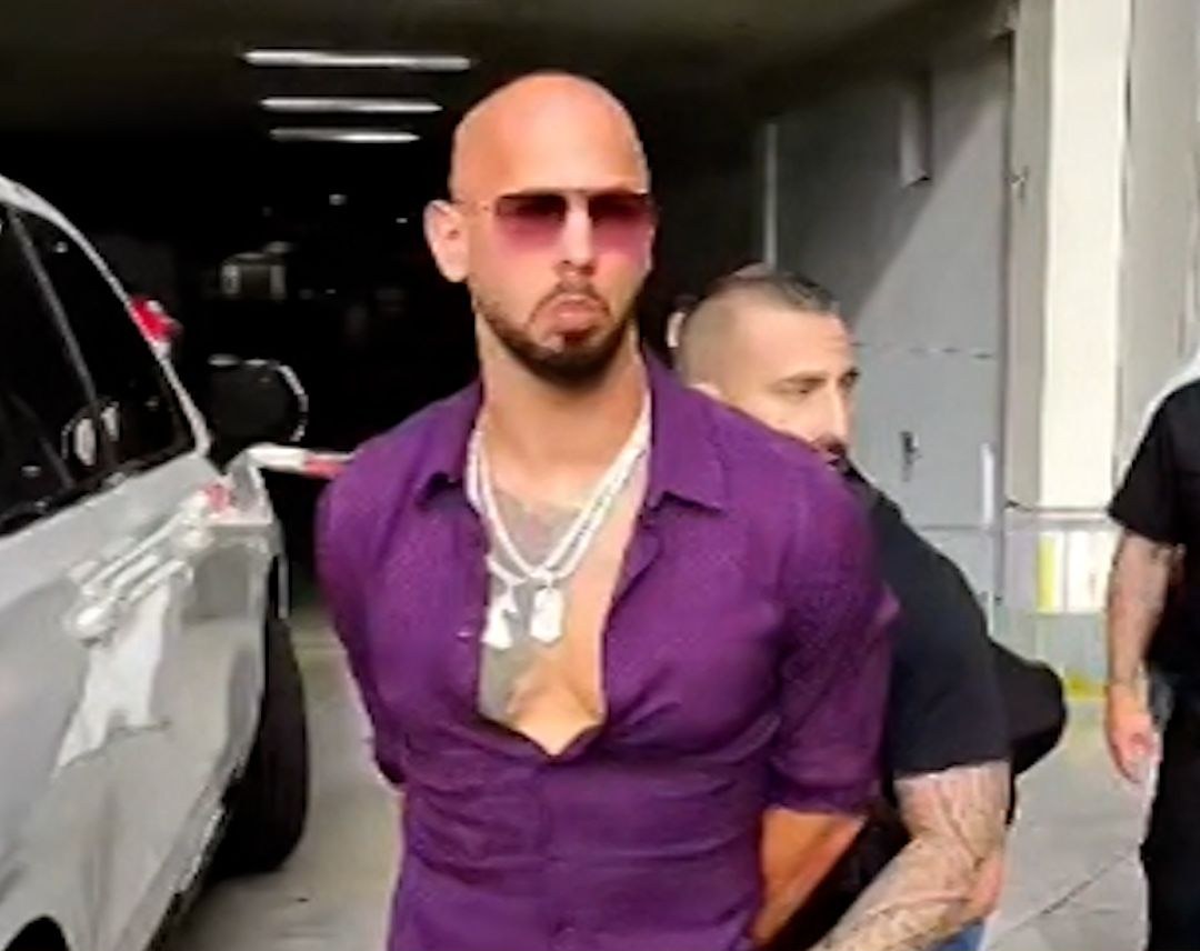 Andrew Tate held by officers beside a vehicle in a Miami parking structure