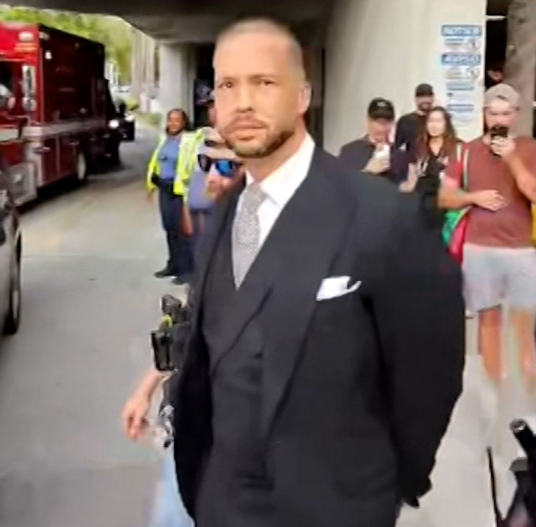 Tristan Tate in a dark suit walking past onlookers in Miami